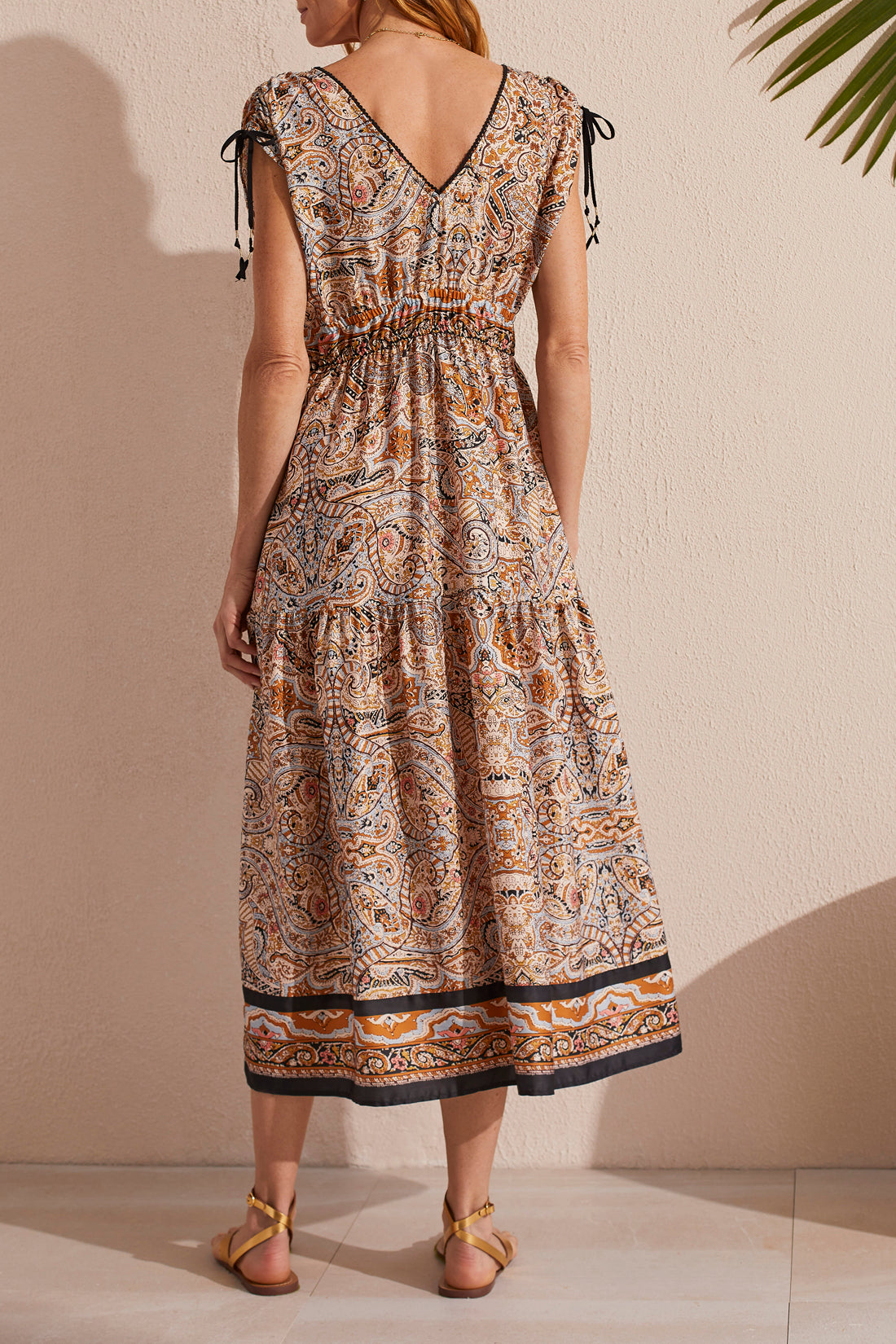 Woman posing in a Tribal Border Print Maxi Dress With Shoulder Ties and waist belt, accessorized with gold sandals.