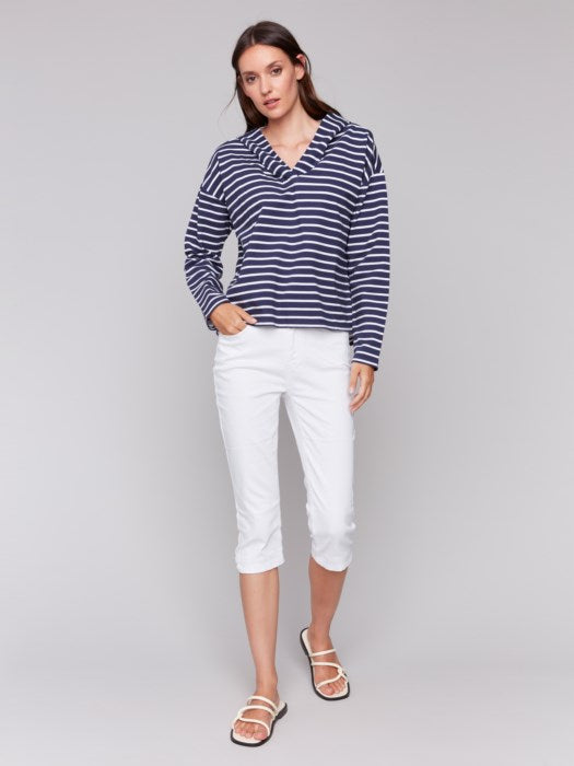 A person in a Charlie B Striped French Terry Hoodie and white capri pants stands against a plain backdrop, hands by their sides.