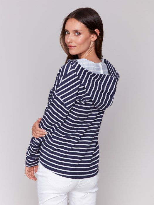 A person in a Charlie B Striped French Terry Hoodie and white capri pants stands against a plain backdrop, hands by their sides.