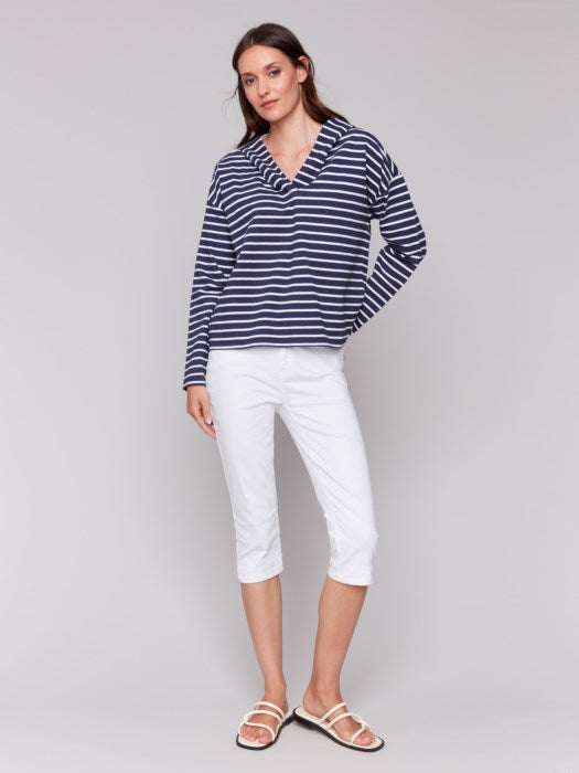 A person in a Charlie B Striped French Terry Hoodie and white capri pants stands against a plain backdrop, hands by their sides.