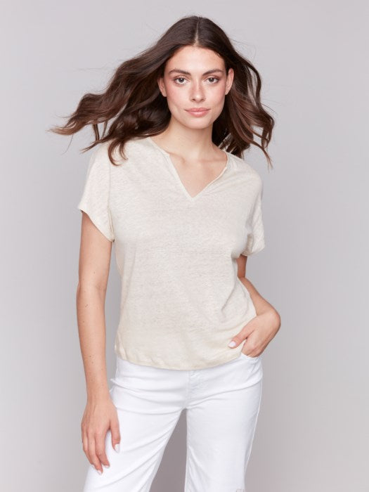 A person with long dark hair wears a stylish V-neck Foil Print Short Sleeve Dolman Top by Charlie B and white pants, posing against a plain background.