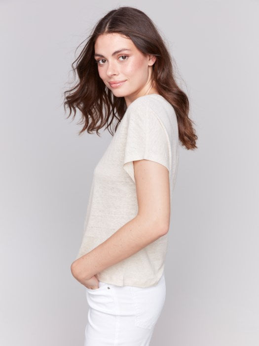 A person with long dark hair wears a stylish V-neck Foil Print Short Sleeve Dolman Top by Charlie B and white pants, posing against a plain background.