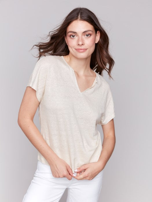 A person with long dark hair wears a stylish V-neck Foil Print Short Sleeve Dolman Top by Charlie B and white pants, posing against a plain background.