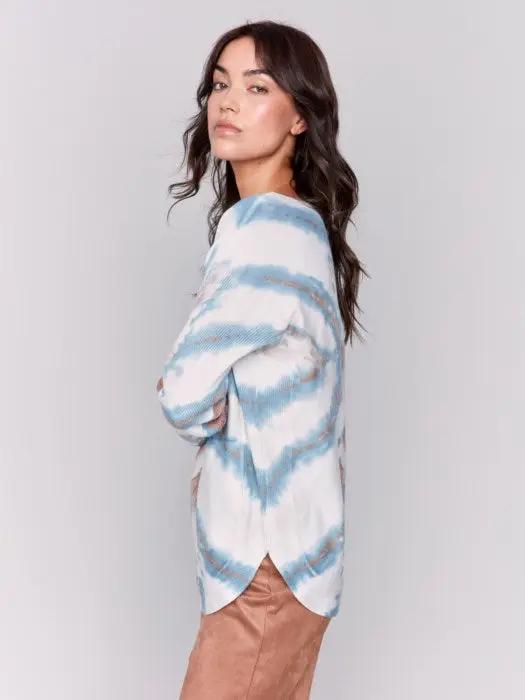 Person with long dark hair facing away from the camera, wearing a cozy and trendy Charlie B Plushy Knit Crew Sweater in a blue and brown tie-dye pattern and brown pants.