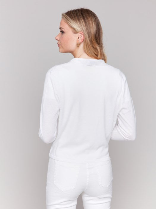 A person with long blonde hair is wearing a stylish white "Tie Front Bolero" top and pants by Charlie B, standing against a plain background, looking towards the camera.