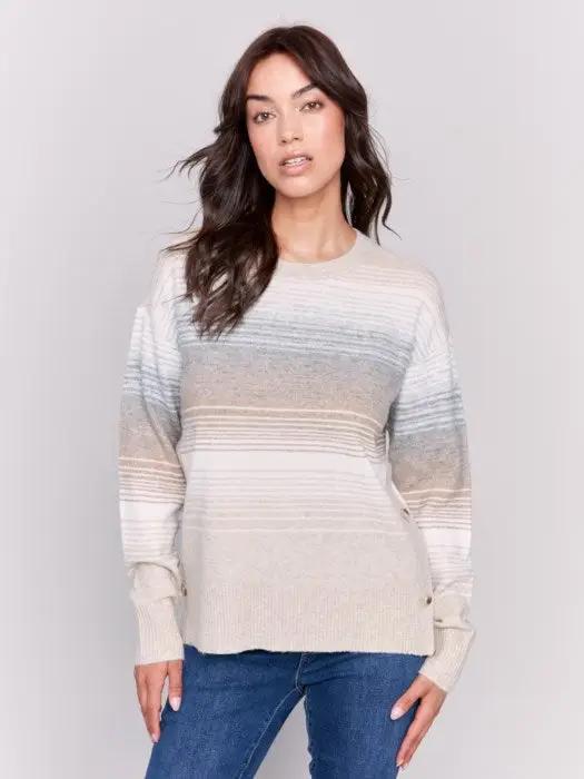 A woman wearing Charlie B's fashion-forward Crew Neck With Side Buttons, a striped long-sleeve sweater in light colors. She has long, wavy dark hair and is posing against a plain white background.