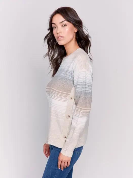 A woman wearing Charlie B's fashion-forward Crew Neck With Side Buttons, a striped long-sleeve sweater in light colors. She has long, wavy dark hair and is posing against a plain white background.