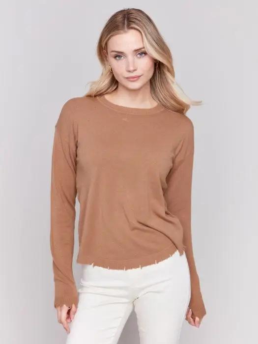 A woman wearing a stylish Round Hem Sweater by Charlie B and white pants stands against a plain background, perfect for cozy nights in.