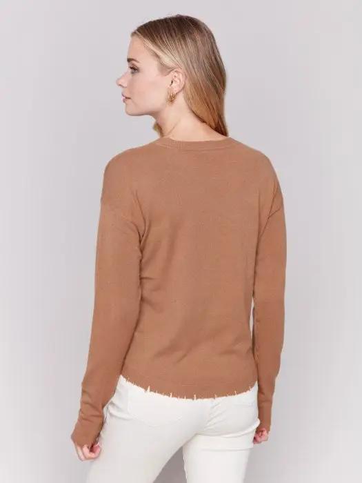 A woman wearing a stylish Round Hem Sweater by Charlie B and white pants stands against a plain background, perfect for cozy nights in.