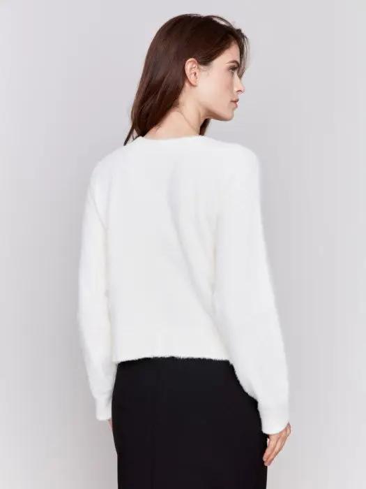 A person is styled in a cozy comfort white ensemble from Charlie B, consisting of a Short Fuzzy Knit Cardigan with buttons and paired with black pants, posed against a plain background while looking to the side with a slight smile, perfectly encapsulating this must-have wardrobe piece.