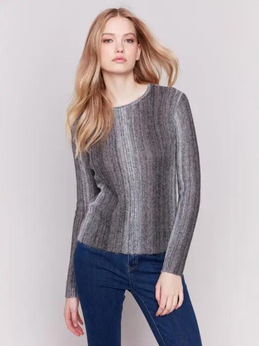 A person with long hair wearing a cozy Space Dye Yarn Crop Sweater by Charlie B and blue jeans stands against a plain background.