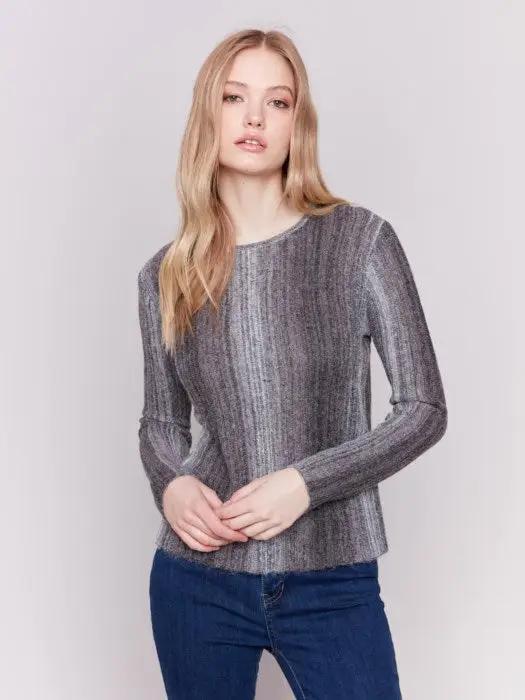 A person with long hair wearing a cozy Space Dye Yarn Crop Sweater by Charlie B and blue jeans stands against a plain background.