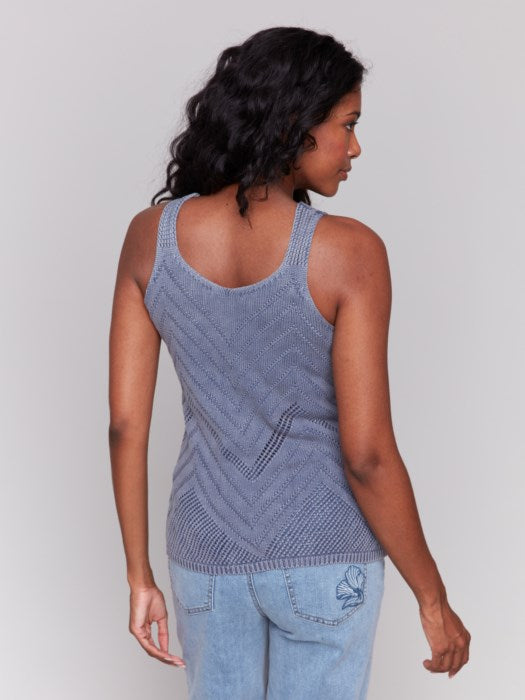 A person smiles, dressed in a chic Charlie B Chevron Pointelle Knit Camisole and light blue jeans, set against a gray background.