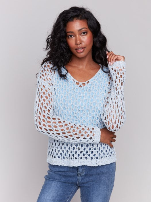 A person wearing the Charlie B Braided Fishnet V-Neck Sweater in light blue with jeans stands against a plain gray background.