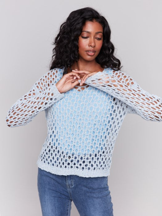 A person wearing the Charlie B Braided Fishnet V-Neck Sweater in light blue with jeans stands against a plain gray background.