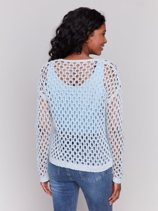 A person wearing the Charlie B Braided Fishnet V-Neck Sweater in light blue with jeans stands against a plain gray background.