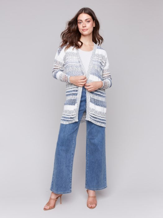 A woman with long brown hair is wearing Charlie B's cozy Knee Length Striped Open Cardigan and jeans, looking back over her shoulder against a plain background.