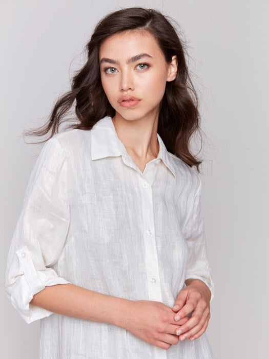 Wearing a Foil Print Linen Blend Tunic Dress by Charlie B over a black top and denim shorts, the woman in a summer outfit poses against a gray background, stylishly finished with white sandals.