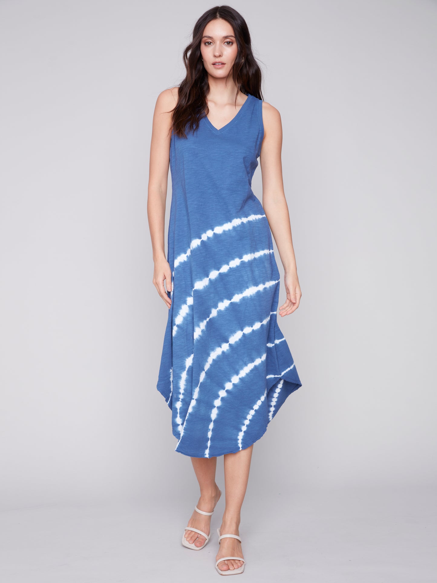 Woman posing in a Charlie B Tie Dye Elegance Dress featuring a blue and white tie-dye pattern and sleeveless design, complemented with sandals.