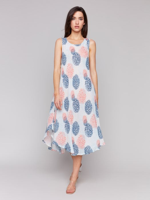 Against a plain backdrop, someone showcases Charlie B’s Sleeveless Printed Rayon Dress, featuring breathable rayon fabric and a charming blue and pink floral pattern with an asymmetrical hemline.