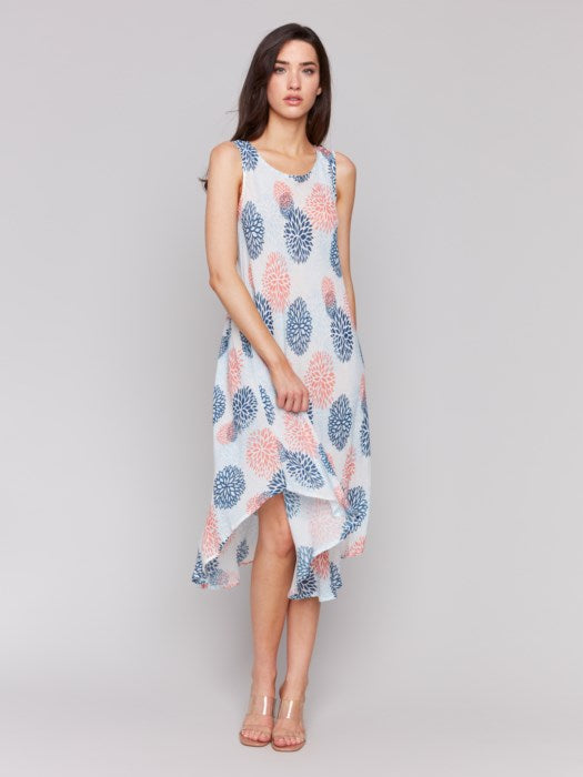 Against a plain backdrop, someone showcases Charlie B’s Sleeveless Printed Rayon Dress, featuring breathable rayon fabric and a charming blue and pink floral pattern with an asymmetrical hemline.