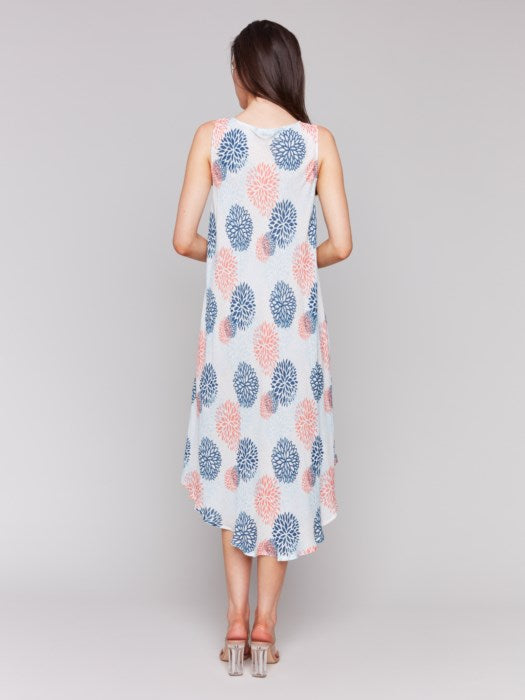 Against a plain backdrop, someone showcases Charlie B’s Sleeveless Printed Rayon Dress, featuring breathable rayon fabric and a charming blue and pink floral pattern with an asymmetrical hemline.