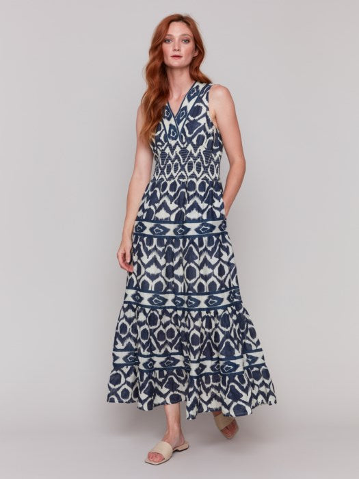 A person is wearing a Charlie B Sleeveless Cotton Maxi Dress with blue and white patterns and ruffled tiers, ideal as a breathable summer dress, against a plain gray background.