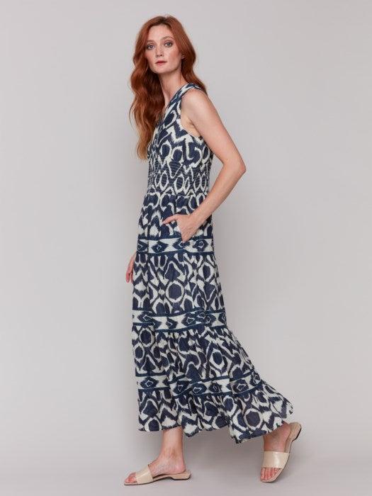 A person is wearing a Charlie B Sleeveless Cotton Maxi Dress with blue and white patterns and ruffled tiers, ideal as a breathable summer dress, against a plain gray background.