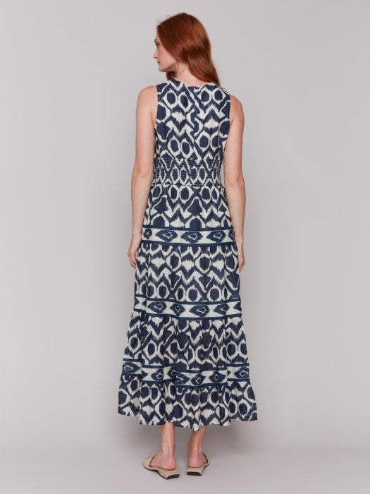 A person is wearing a Charlie B Sleeveless Cotton Maxi Dress with blue and white patterns and ruffled tiers, ideal as a breathable summer dress, against a plain gray background.