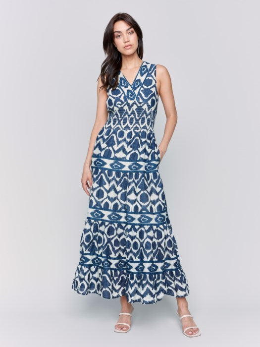 A person is wearing a Charlie B Sleeveless Cotton Maxi Dress with blue and white patterns and ruffled tiers, ideal as a breathable summer dress, against a plain gray background.