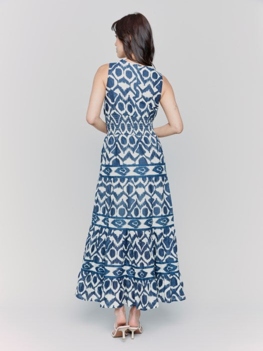 A person is wearing a Charlie B Sleeveless Cotton Maxi Dress with blue and white patterns and ruffled tiers, ideal as a breathable summer dress, against a plain gray background.