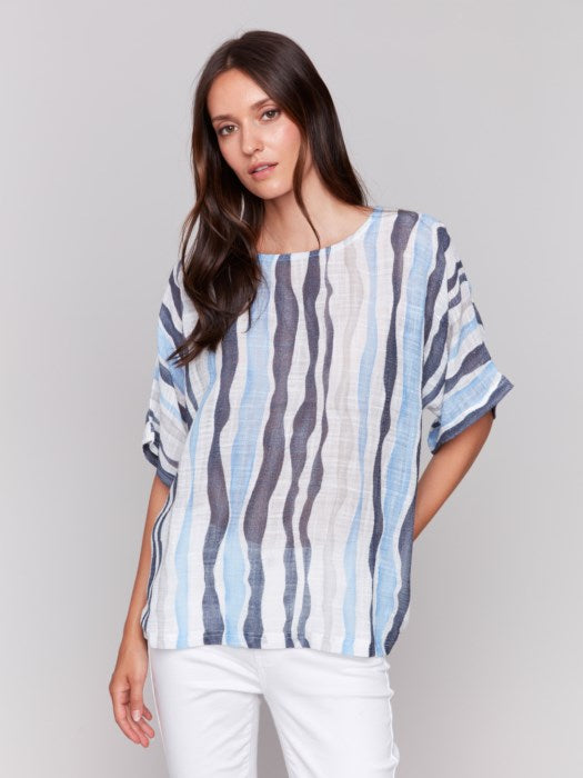 A person models Charlie B's Cotton Gauze Dolman Top in blue and white, paired with white pants against a gray background, capturing the summer vibe with its airy fabric.