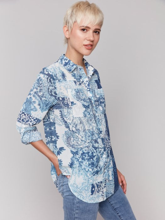 A person with short blond hair is wearing a Charlie B Printed Crinkle Button-Front Blouse in blue and white, paired with jeans, standing against a plain background.