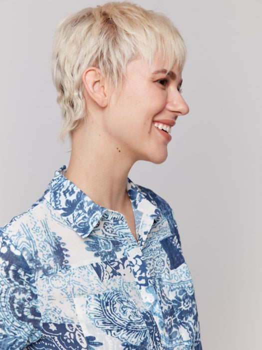 A person with short blond hair is wearing a Charlie B Printed Crinkle Button-Front Blouse in blue and white, paired with jeans, standing against a plain background.