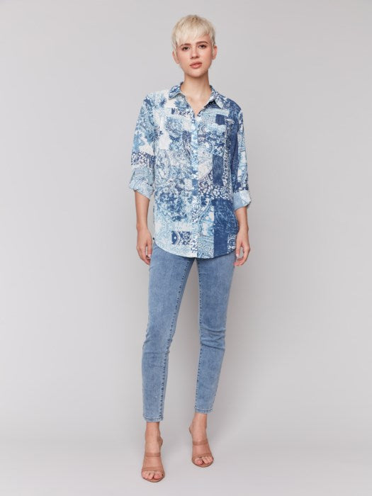 A person with short blond hair is wearing a Charlie B Printed Crinkle Button-Front Blouse in blue and white, paired with jeans, standing against a plain background.