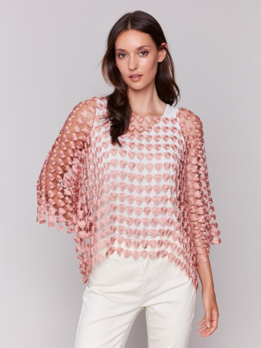 Against a plain backdrop, someone wears Charlie B's Textured Crochet Heart Top, a sheer pink heart-patterned piece layered over a white shirt.