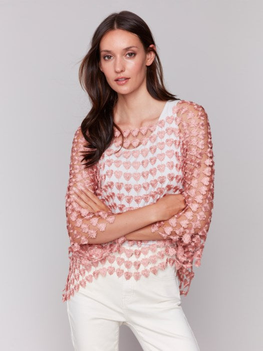 Against a plain backdrop, someone wears Charlie B's Textured Crochet Heart Top, a sheer pink heart-patterned piece layered over a white shirt.