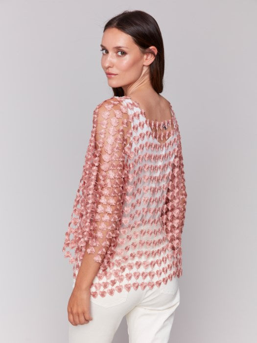 Against a plain backdrop, someone wears Charlie B's Textured Crochet Heart Top, a sheer pink heart-patterned piece layered over a white shirt.