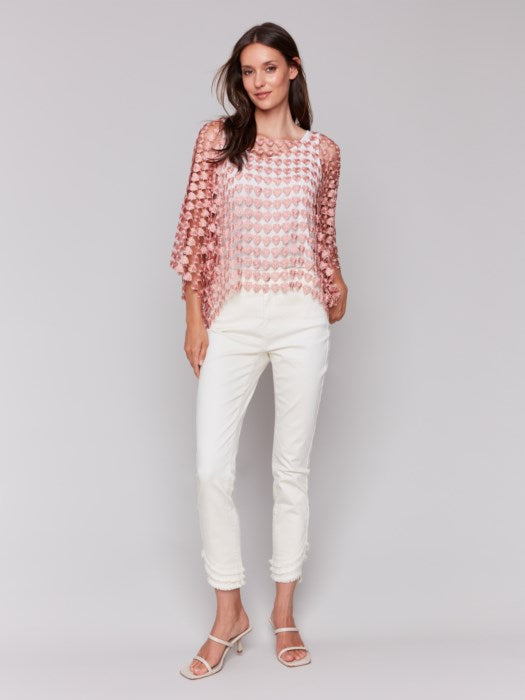 Against a plain backdrop, someone wears Charlie B's Textured Crochet Heart Top, a sheer pink heart-patterned piece layered over a white shirt.