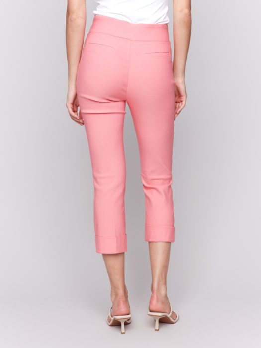 Rear view of someone wearing flattering pink Stretch Pull-On Capri Pants by Charlie B and a white top, standing in heels against a neutral background.