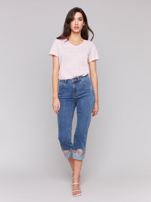 A woman in a pink T-shirt and Charlie B's Embroidered Cuff Cropped Jeans poses against a gray background.