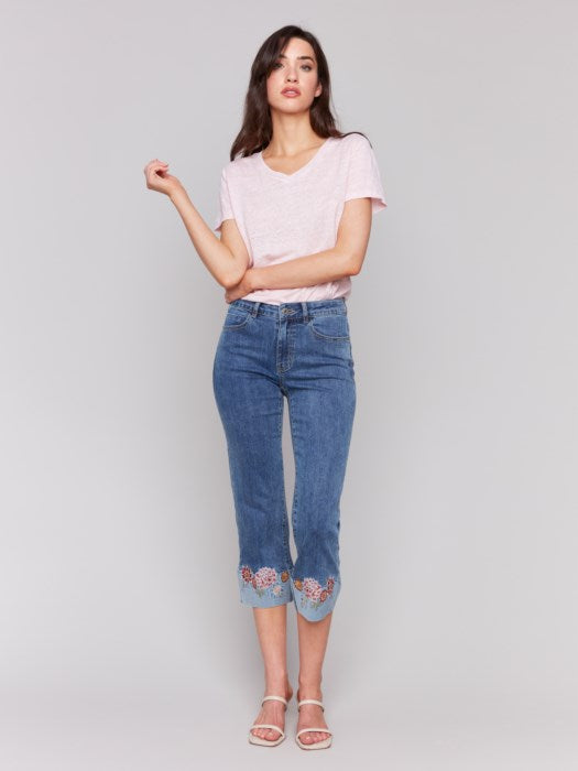 A woman in a pink T-shirt and Charlie B's Embroidered Cuff Cropped Jeans poses against a gray background.