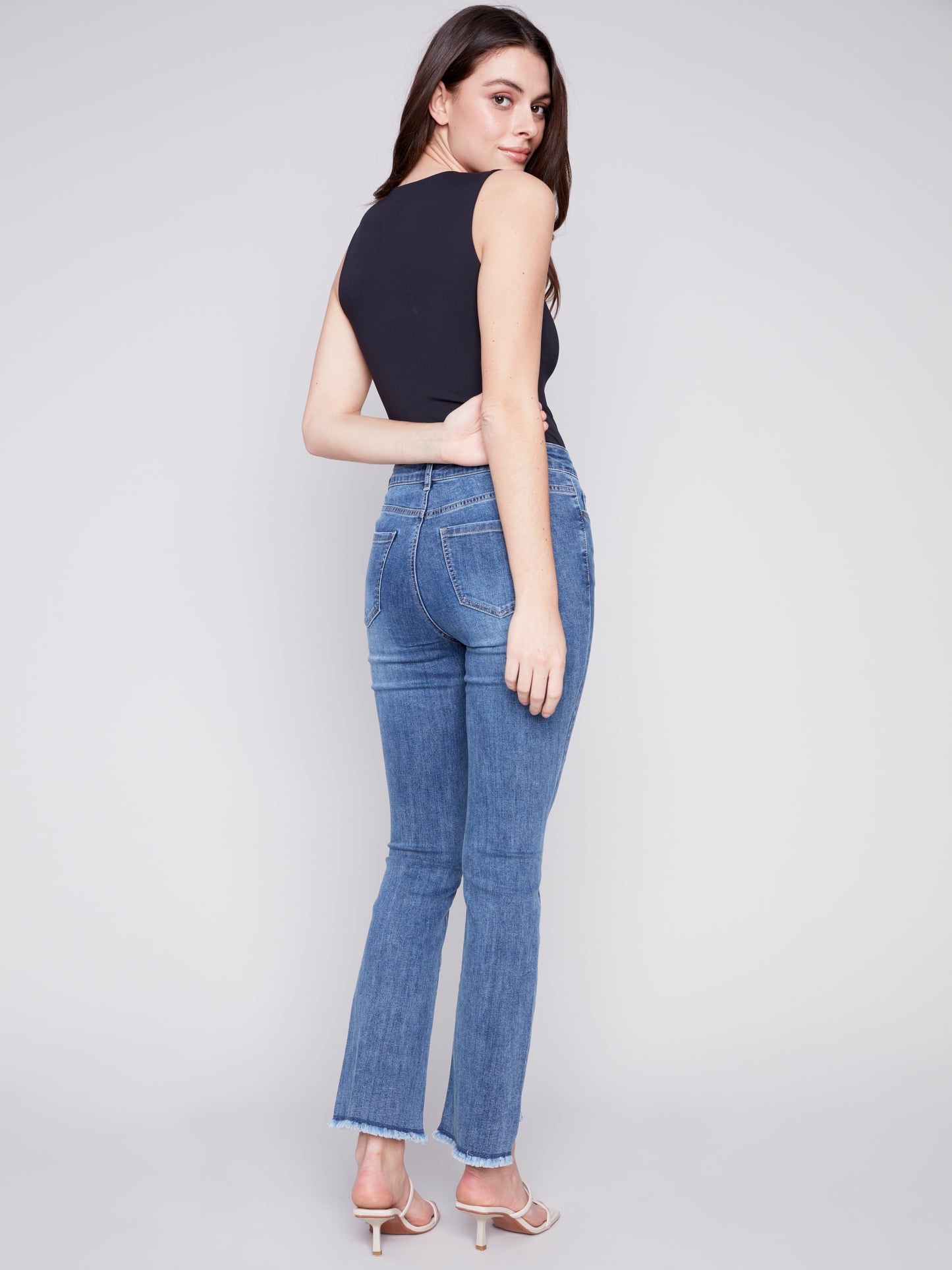 A woman donning a must-have pair of Charlie B Asymmetrical Boot Cut Hem Jeans.