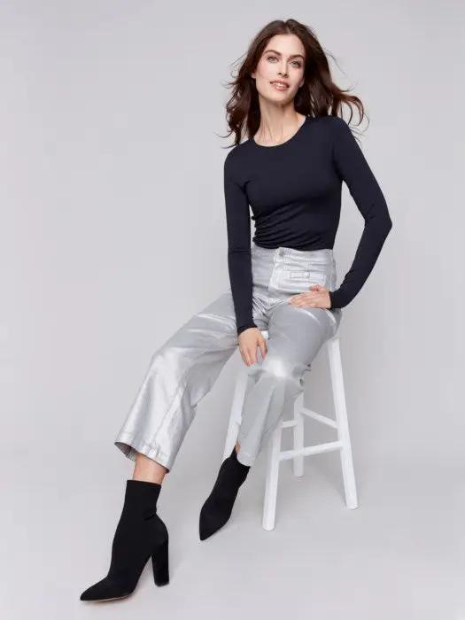 A person sits on a stool wearing a black long-sleeve top, Charlie B's Metallic Wax Flared Pants that shimmer in the light, and black heeled boots against a plain background.