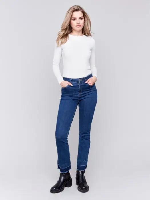 A person in a white long-sleeve shirt wears Charlie B's Ombre Hem Flare Jeans with Studs and black ankle boots. Only the lower part of the body is visible.