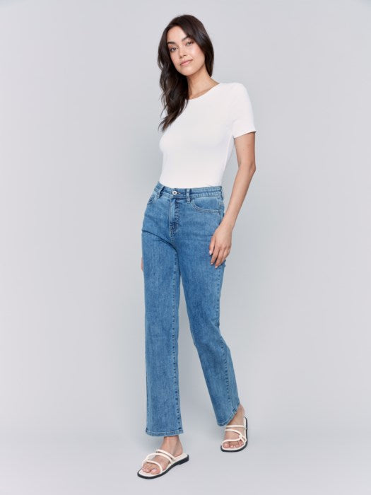 A person wearing Charlotte Straight Leg blue jeans by Charlie B and white sandals, photographed from the back, with a white top tucked for effortless style and comfort.