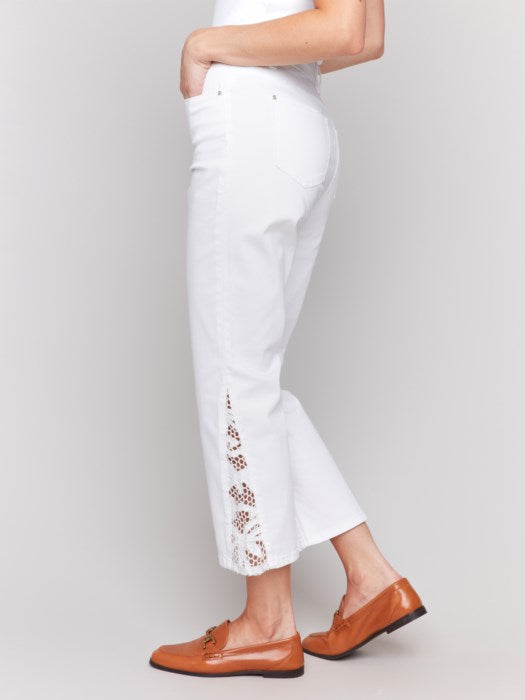 A woman in a white sleeveless top and Charlie B's Lace Cut Side Bootcut Twill Pants with embroidered details stands against a plain background, wearing brown shoes.