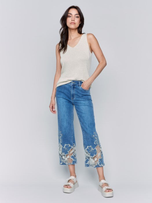 A woman is wearing Charlie B's Crop Flare Leg Jeans with a laser cut lace hem, paired with white platform sandals.