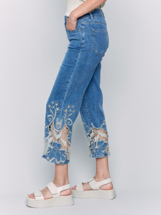 A woman is wearing Charlie B's Crop Flare Leg Jeans with a laser cut lace hem, paired with white platform sandals.