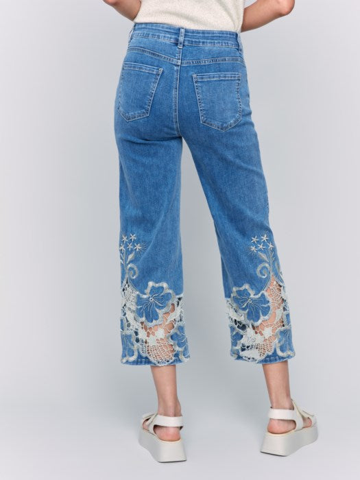 A woman is wearing Charlie B's Crop Flare Leg Jeans with a laser cut lace hem, paired with white platform sandals.